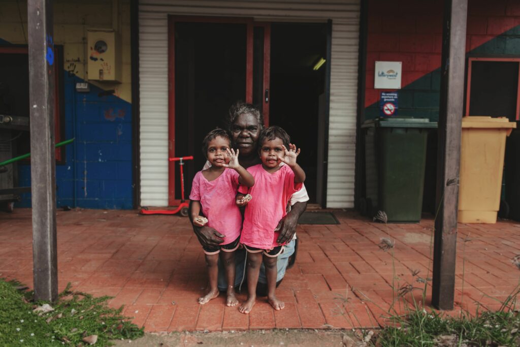 Two young children and a carer in front doors of a building
