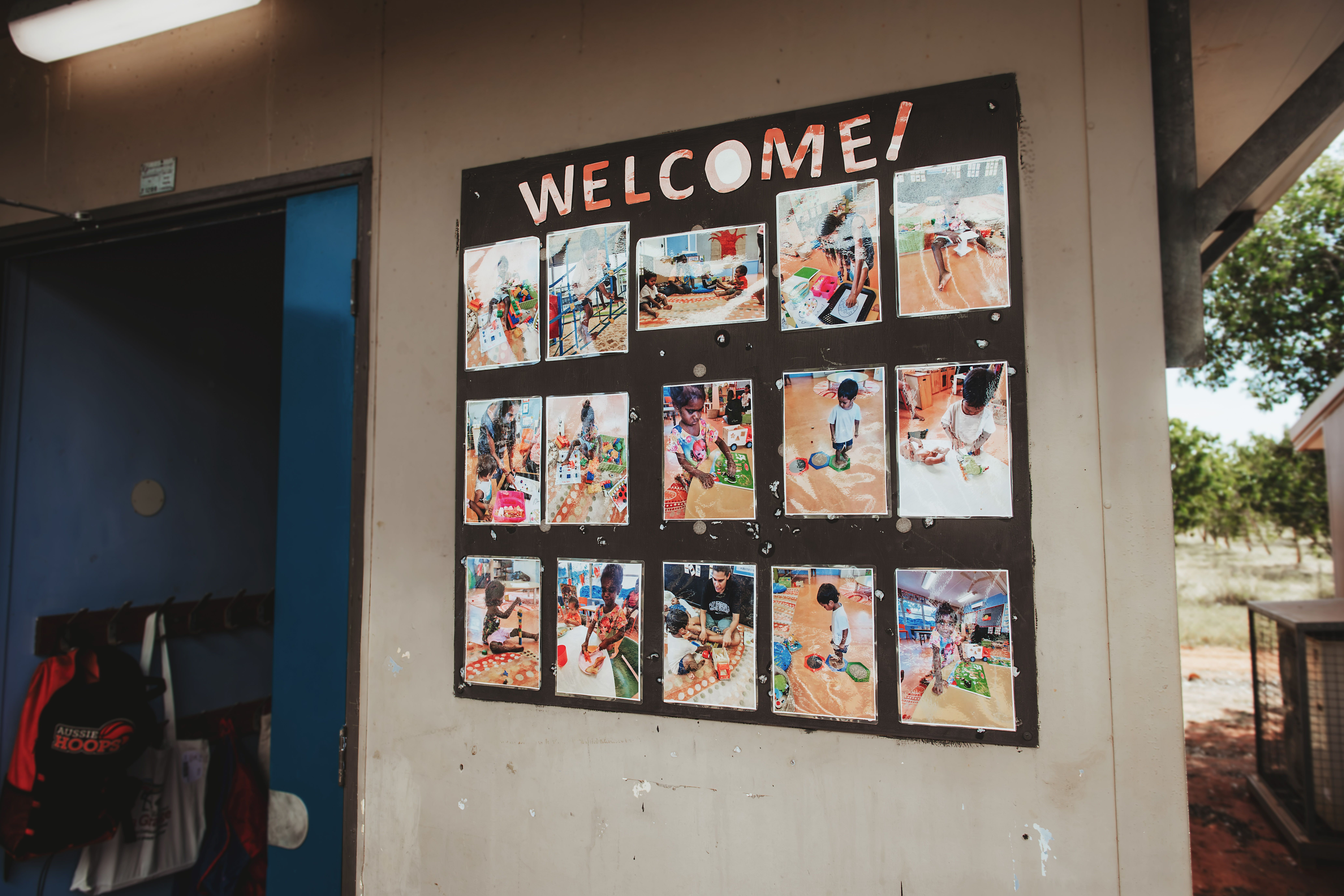 A board with 'Welcome' written across the top, displaying photos of children playing in a classroom