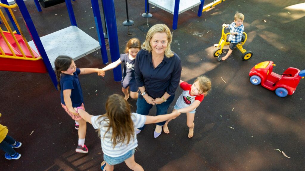 Children holding hands encircle a woman in a playground