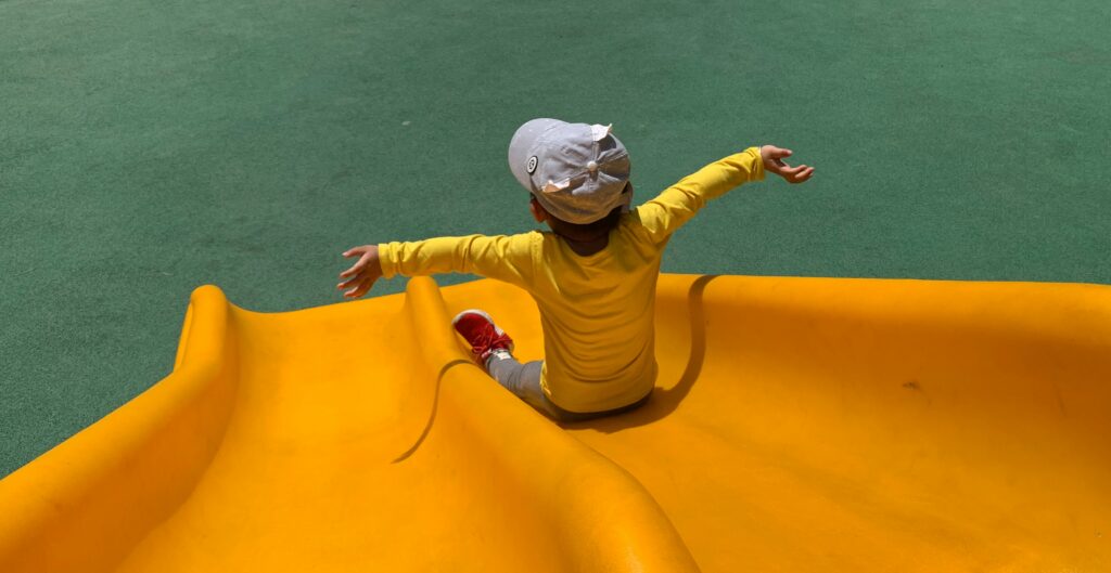 Young child with arms outstretched going down a yellow playground slide